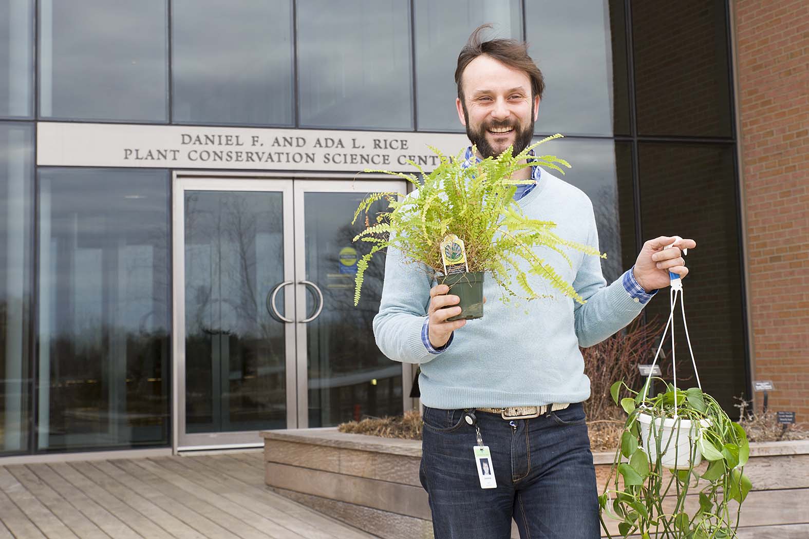 PHOTO: Dr. Fant carries a fern and a pothos plants out of the Plant Conservation Science Center.