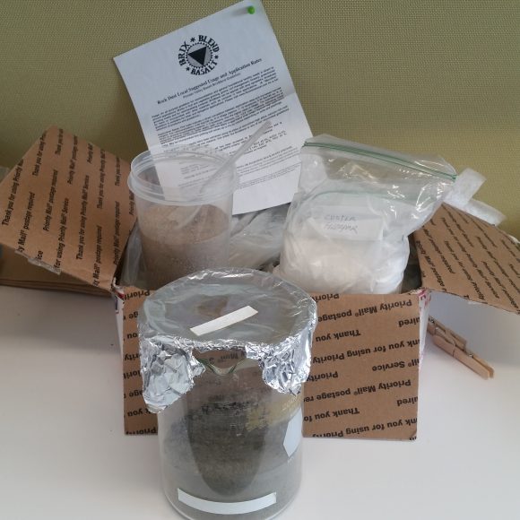 PHOTO: a box of basalt, a cup of sand, a bag of feldspar, and a glass beaker containing the Martian soil mixture