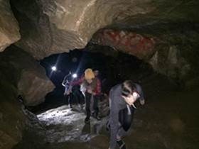 PHOTO: students with flashlights hunched over as they walk through a cave with a low ceiling.