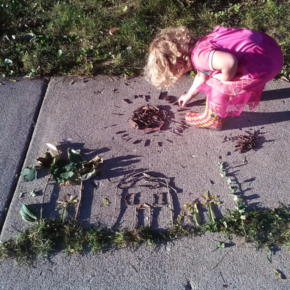 PHOTO: Sticks and grass make a portrait of our house; Laila works on a mulch sun.